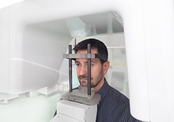 Male patient with dark hair standing inside cone beam scanner