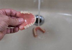Person rinsing their dentures in sink