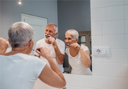 Older couple brushing their teeth in front of mirror