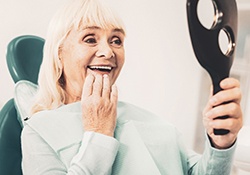 Woman admiring her dentures, glad she could afford treatment