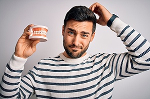 Man in striped shirt, holding dentures and scratching his head