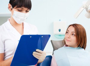 Dental team member standing beside patient, taking notes