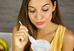 Woman in yellow shirt eating yogurt after oral surgery