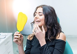 Patient using mirror to admire her new dental implant restorations