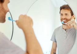 Man brushing his teeth in front of bathroom mirror