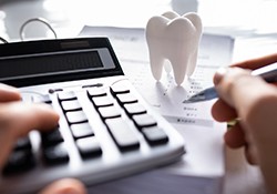 Hands using calculator and pen to budget for dental care