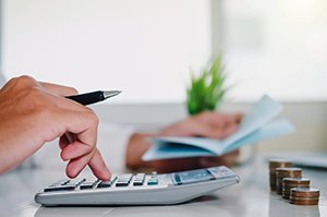 Hand using calculator to budget the cost of teeth whitening