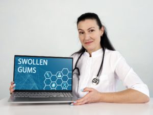 Medical professional holding laptop with “Swollen Gums” displayed on screen