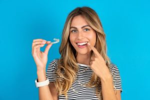 Woman holding Invisalign aligner and pointing at her teeth
