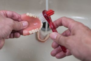 Person brushing their dentures over bathroom sink