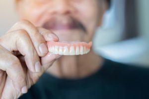 Man in black t-shirt holding upper denture